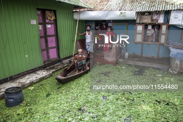 All members of a family stand in front of a flooded house, and an elderly man sits on a boat in a village in Chaumuhani Municipality of Noak...