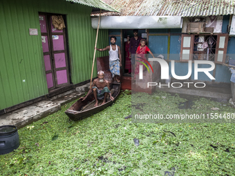 All members of a family stand in front of a flooded house, and an elderly man sits on a boat in a village in Chaumuhani Municipality of Noak...