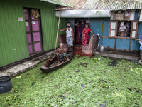 All members of a family stand in front of a flooded house, and an elderly man sits on a boat in a village in Chaumuhani Municipality of Noak...