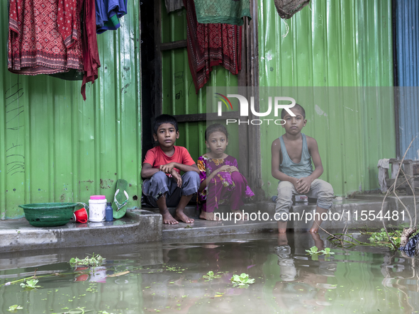 Three children sit in front of their flooded house in a village of Chaumuhni Municipality in Noakhali District in Chittagong, Bangladesh, on...