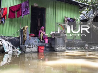 A woman cooks on high ground in front of her flooded house in a village in Chaumuhani Municipality of Noakhali District, Chittagong Division...