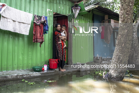 A woman holds a small child in her arms in front of her flooded house in a village in Chaumuhani Municipality of Noakhali District, Chittago...