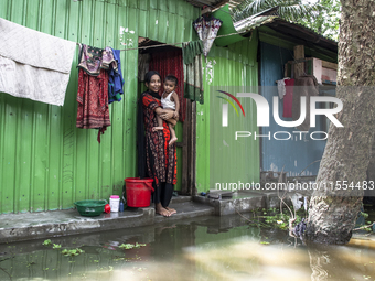 A woman holds a small child in her arms in front of her flooded house in a village in Chaumuhani Municipality of Noakhali District, Chittago...