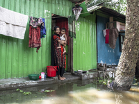 A woman holds a small child in her arms in front of her flooded house in a village in Chaumuhani Municipality of Noakhali District, Chittago...