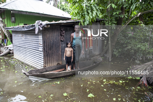 A man and his child stand on a boat, the only means of transport, in front of their flooded house in a village in Chaumuhni Municipality, No...