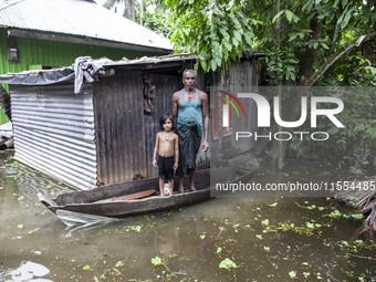 A man and his child stand on a boat, the only means of transport, in front of their flooded house in a village in Chaumuhni Municipality, No...