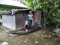 A man and his child stand on a boat, the only means of transport, in front of their flooded house in a village in Chaumuhni Municipality, No...