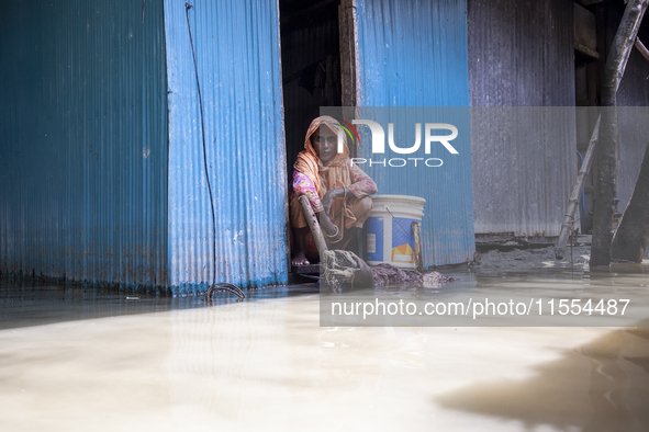 A woman sits in front of her flooded house in a village in Choumuhani Municipality of Noakhali District in Chittagong Division, Bangladesh,...