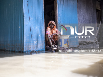 A woman sits in front of her flooded house in a village in Choumuhani Municipality of Noakhali District in Chittagong Division, Bangladesh,...