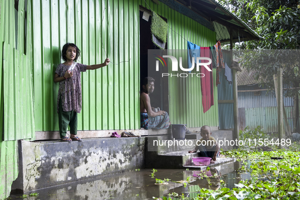 A man and his young children sit in front of their flooded house in a village in Choumuhani Municipality of Noakhali District in Chittagong...