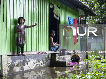 A man and his young children sit in front of their flooded house in a village in Choumuhani Municipality of Noakhali District in Chittagong...