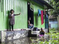 A man and his young children sit in front of their flooded house in a village in Choumuhani Municipality of Noakhali District in Chittagong...