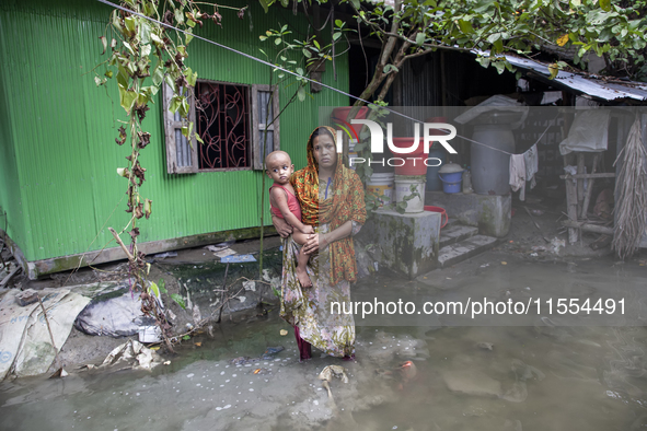 A woman holds a small child in her arms in front of her flooded house in a village in Chaumuhani Municipality of Noakhali District, Chittago...