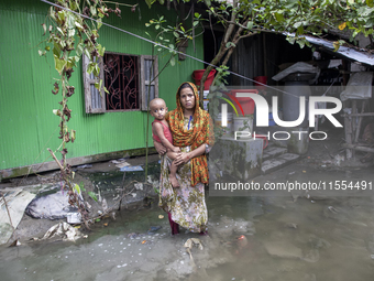 A woman holds a small child in her arms in front of her flooded house in a village in Chaumuhani Municipality of Noakhali District, Chittago...