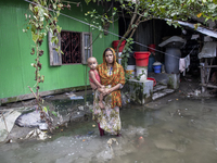 A woman holds a small child in her arms in front of her flooded house in a village in Chaumuhani Municipality of Noakhali District, Chittago...