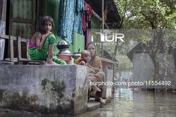 A mother and her children sit in front of their flooded house in a village in Chaumuhani Municipality of Noakhali District in Chittagong Div...