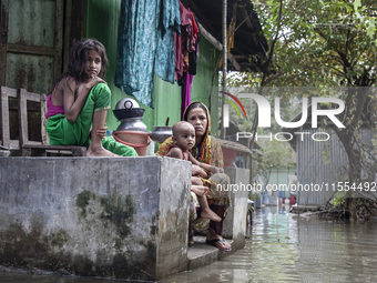 A mother and her children sit in front of their flooded house in a village in Chaumuhani Municipality of Noakhali District in Chittagong Div...