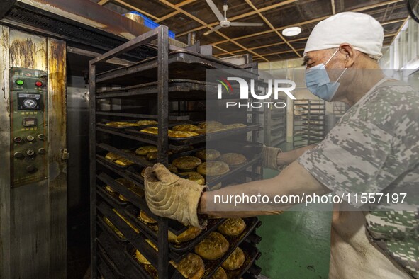 A worker takes a mooncake out of an electric oven at the production workshop of Dongfang Pastry Co., LTD., a time-honored pastry company in...