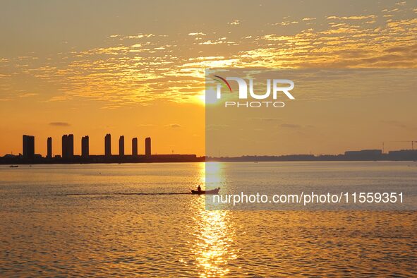 A fishing boat rides in Tangdao Bay illuminated by the rising sun in Qingdao, China, on September 9, 2024. 