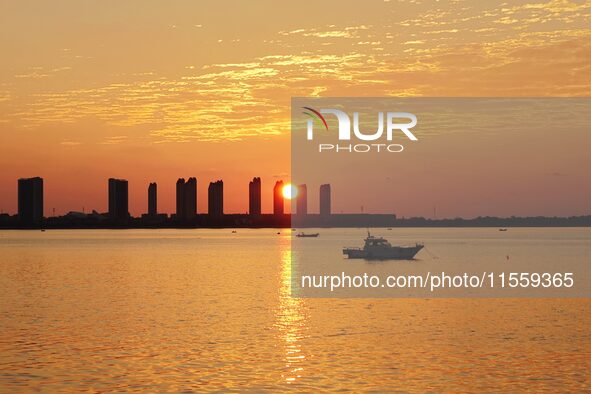 A fishing boat rides in Tangdao Bay illuminated by the rising sun in Qingdao, China, on September 9, 2024. 