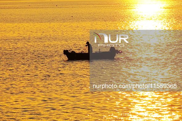 A fishing boat rides in Tangdao Bay illuminated by the rising sun in Qingdao, China, on September 9, 2024. 