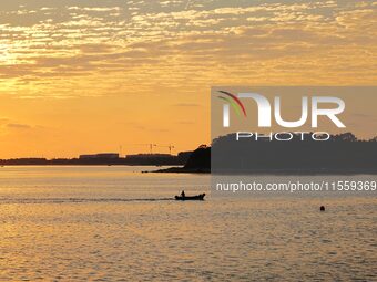 A fishing boat rides in Tangdao Bay illuminated by the rising sun in Qingdao, China, on September 9, 2024. (