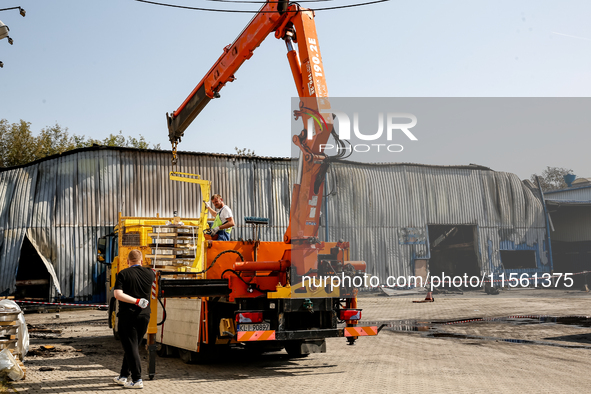 People collect debris in front of burned warehouse in southern Krakow as it burned in the night on September 7, 2024 in Krakow, Poland. This...