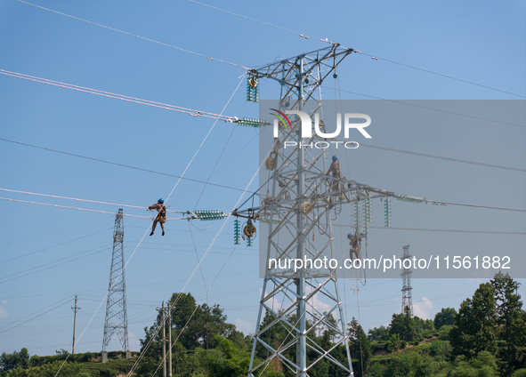 Electric power employees work on a steel tower near the Shuigang Railway in Xikouping village, Yichang city, Central China's Hubei province,...