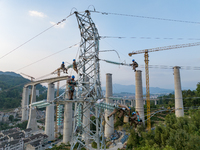 Electric power employees work on a steel tower near the Shuigang Railway in Xikouping village, Yichang city, Central China's Hubei province,...