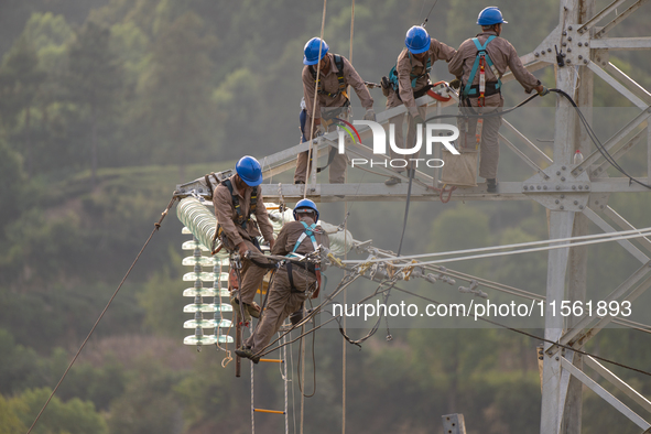 Electric power employees work on a steel tower near the Shuigang Railway in Xikouping village, Yichang city, Central China's Hubei province,...