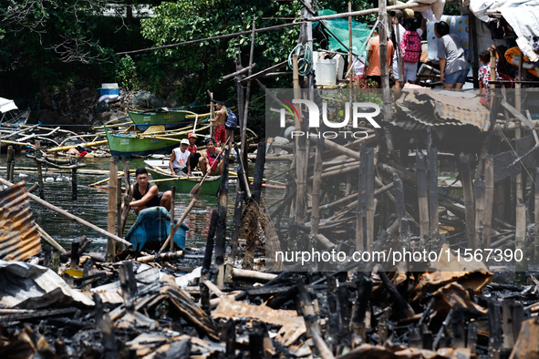 People on boats paddle near the rubble of damaged houses following a huge fire that engulfs at least 800 houses in Bacoor, Cavite, the Phili...