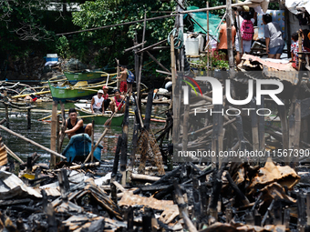 People on boats paddle near the rubble of damaged houses following a huge fire that engulfs at least 800 houses in Bacoor, Cavite, the Phili...