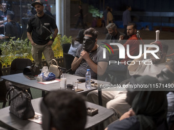 Iranian youths hold masks in front of their faces while playing Mafia, a party game, at a cafe at Adrenaline Park in Tehran, Iran, on Septem...