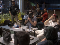 Iranian youths hold masks in front of their faces while playing Mafia, a party game, at a cafe at Adrenaline Park in Tehran, Iran, on Septem...