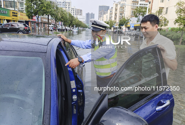 A traffic policeman helps citizens deal with stranded vehicles after a rainstorm in Huai'an, China, on September 14, 2024. 