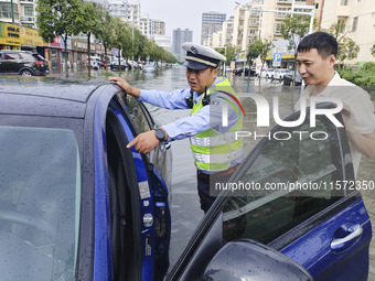 A traffic policeman helps citizens deal with stranded vehicles after a rainstorm in Huai'an, China, on September 14, 2024. (