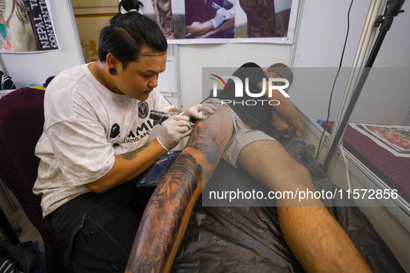 An artist (L) inks a tattoo on the body of an enthusiast (R) during the Himalayan Tattoo Convention in Lalitpur, Nepal, on August 14, 2024....