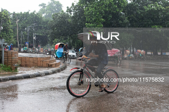 A cyclist holds an umbrella while riding in the rain in Dhaka, Bangladesh, on September 15, 2024. 