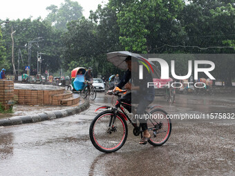 A cyclist holds an umbrella while riding in the rain in Dhaka, Bangladesh, on September 15, 2024. (