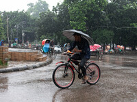 A cyclist holds an umbrella while riding in the rain in Dhaka, Bangladesh, on September 15, 2024. (