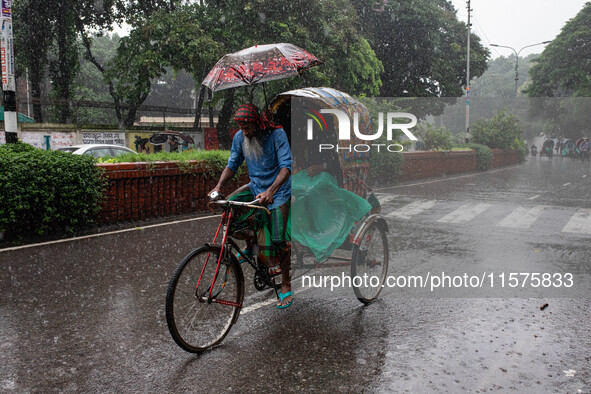 A passenger holds an umbrella to protect himself and the rickshaw puller as rain continues in Dhaka, Bangladesh, on September 15, 2024. 