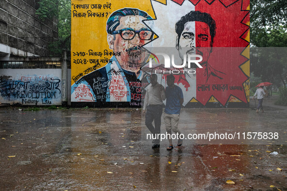 People walk in the rain in front of the wall, where Siraj Sikder's graffiti is next to Sheikh Mujibur Rahman's graffiti, calling him the kil...