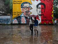 People walk in the rain in front of the wall, where Siraj Sikder's graffiti is next to Sheikh Mujibur Rahman's graffiti, calling him the kil...