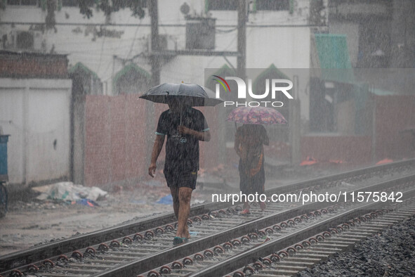 Two people walk on the railway line with umbrellas in the heavy rain in Dhaka, Bangladesh, on September 15, 2024. 