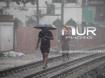 Two people walk on the railway line with umbrellas in the heavy rain in Dhaka, Bangladesh, on September 15, 2024. (