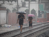 Two people walk on the railway line with umbrellas in the heavy rain in Dhaka, Bangladesh, on September 15, 2024. (