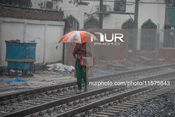 A woman walks on the railway line with umbrellas in the heavy rain in Dhaka, Bangladesh, on September 15, 2024. 