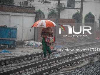 A woman walks on the railway line with umbrellas in the heavy rain in Dhaka, Bangladesh, on September 15, 2024. (