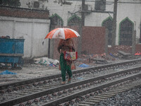 A woman walks on the railway line with umbrellas in the heavy rain in Dhaka, Bangladesh, on September 15, 2024. (