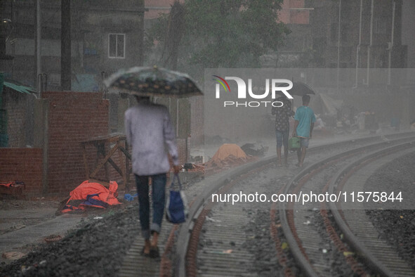 People walk on the railway line with umbrellas in the heavy rain in Dhaka, Bangladesh, on September 15, 2024. 